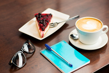 close up of notebook with pen, coffee cup and cake