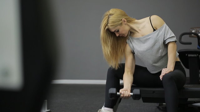 A woman athlete doing exercise on the biceps in the arm straining their muscles, lifting dumbbell in the gym, with muscular body.