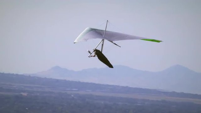 Hang glider soaring through air with valley and mountains seen in distance.