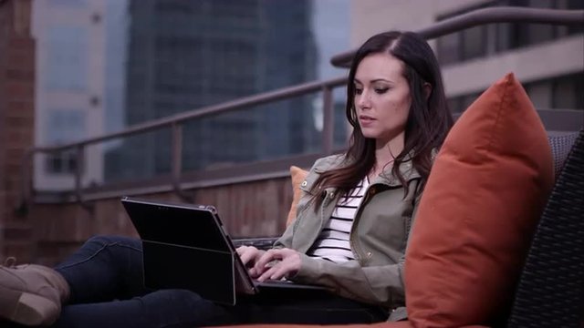 Up close view of woman relaxing on roof top typing on laptop running fingers through hair.