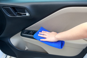 Woman hand cleaning interior car door panel with microfiber clot