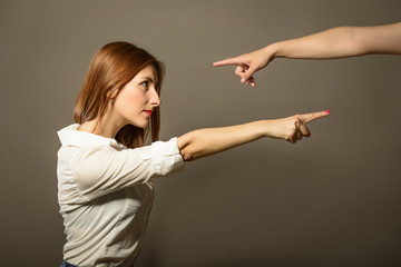 Beautiful woman point finger on someone while someone else pointing finger on her, studio shot on gray background. Side profile portrait of angry upset person, blaming other. Negative human emotion