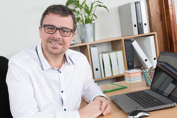 Fototapeta na wymiar Man, wearing glasses and smiling, as he works on laptop