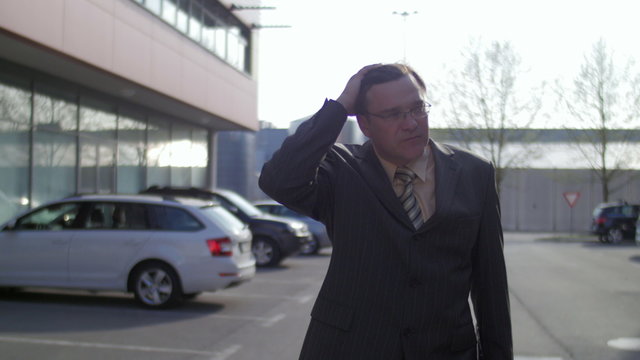 Sad business man walking in a parking lot between buildings