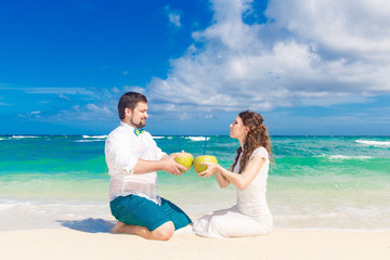 Happy bride and groom having fun on a tropical beach with coconu