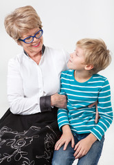 Caucasian elderly woman and young boy together looking each other, portrait on a gray background