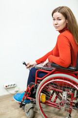 Fototapeta na wymiar Disabled Caucasian woman sitting wheelchair with power plug in hand and looking at camera