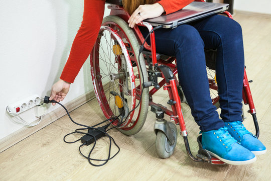 Unrecognizable woman inserting laptop plug with her hand in power socket, disabled person in wheelchair