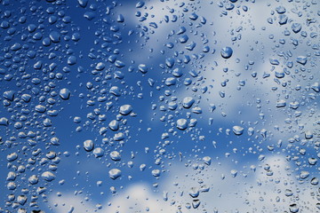 Rain drops on window with blue cloudy sky in background