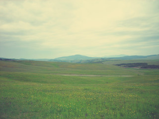 Early spring landscape in the countryside on a cloudy day; green fields and hills. Image filtered in faded, retro, Instagram style with soft focus; nostalgic vintage concept of spring.