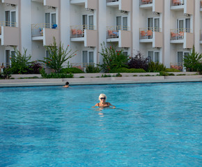 Aged lady is in bright blue water of swimming pool.