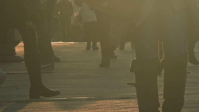 Unrecognizable crowd of people walking on city street in sunset, silhouettes of people and shadows on pavement.