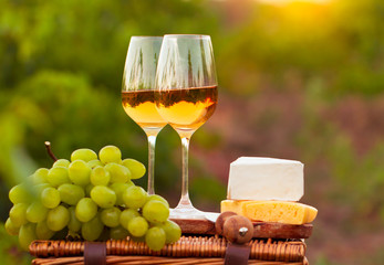 Two glasses white wine, various sorts of cheese and grapes on th
