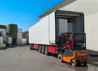 Worker on loader loads white semi-truck
