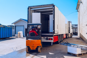 Worker on the loader loads long white semi-truck