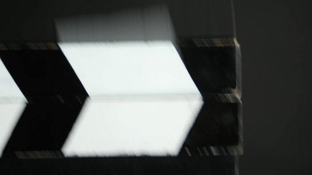 Person uses movie clapper board, on black, close up