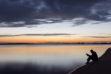 Naklejka na ściany i meble Silhouette of man reading near to lake at sunset