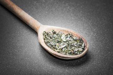 Green tea on wooden spoon isolated on black.