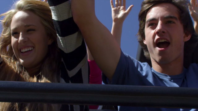 Slow motion shot of couple rasing arms in air while riding rollercoaster.
