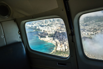 View from an airplane window on the city of Honolulu with Waikiki beach - Hawaii, USA. Selective focus on the airplane interior. Photo taken on a small commuter plane on the way from Oahu to Maui.