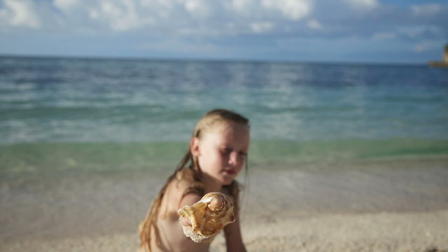Child holding a seashell on the beach