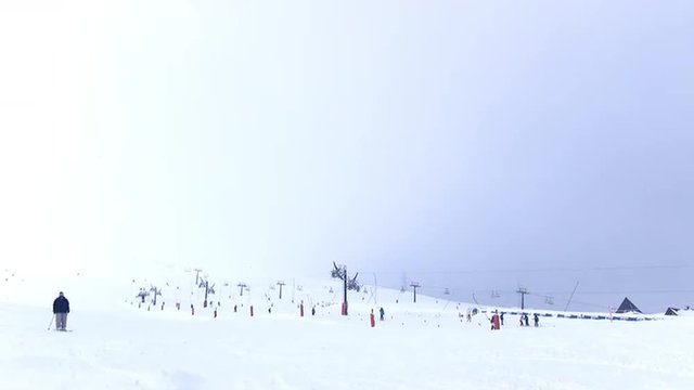 An isolated skier passing in front of the camera in slow motion - ski tows in background with a few people - mist on the station and in the mountains.