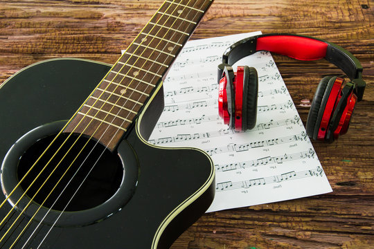 Acoustic guitar, headphones and sheet musical noteson the table.