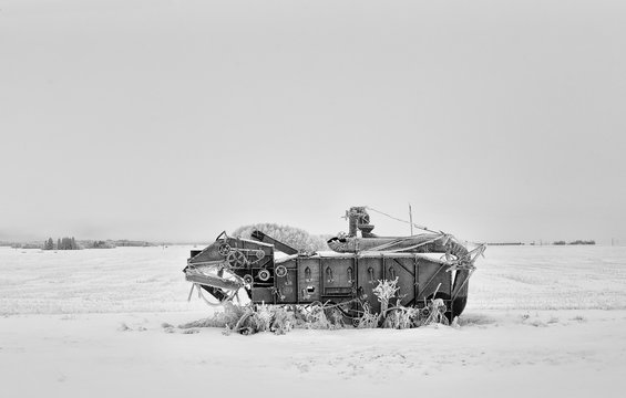 Vintage agricultural threshing machine in a black and white winter landscape