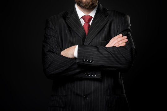 man dressed in strict suit folded arms. Black background