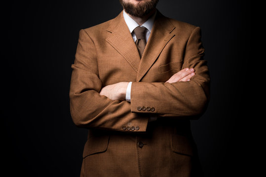 man dressed in strict suit folded arms. Black background