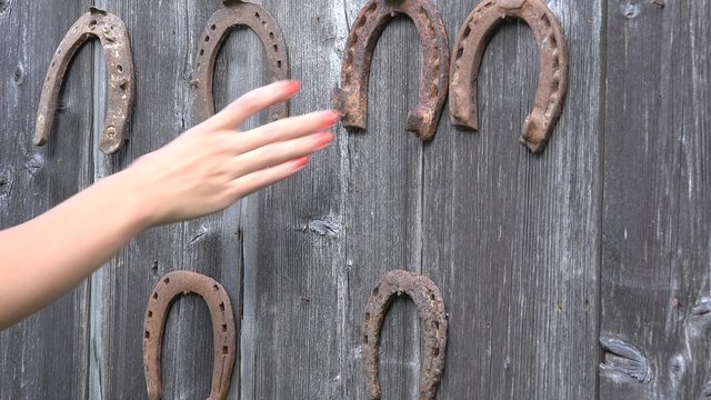 Girl hand put retro rusty horseshoes hanging on old wooden rural house wall.  Static closeup shot. 4K
