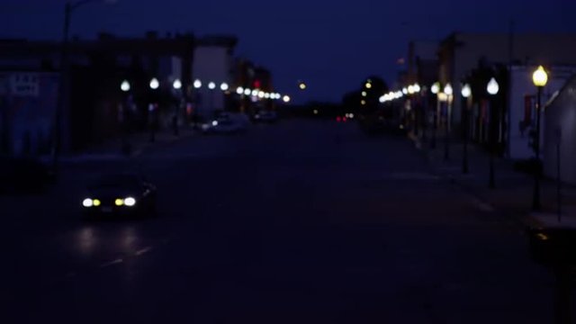 Street view at night with rack focus as a car drives down the street.