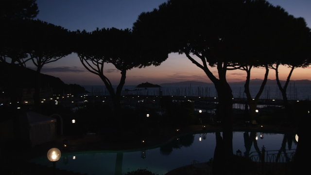 Zoom out to silhouetted of trees with sunset in Punta Ala Italy.