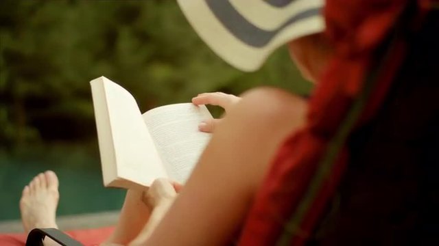 An older woman sitting by the pool reading a book, in slow motion