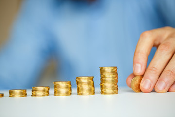 Male hand stacking gold coins into increasing columns