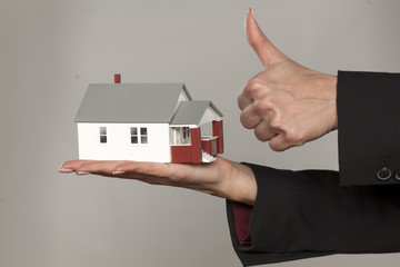 female hands holding a model house and showing thumbs up