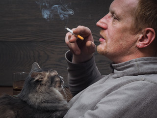Мужчина отдыхает. На коленях кот, в руках сигарета, на столе стакан с алкоголем. Мужские радости или вредные привычки