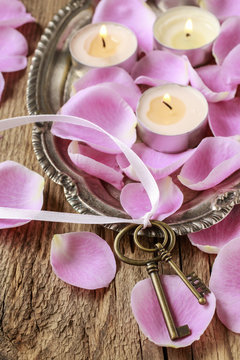 Romantic vintage keys and scented candles among pink rose petals