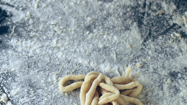 Female hands lay out pasta pici over black table, powdering by flour