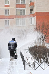 man removes snow in the yard of a multistory building with snow