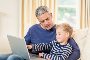 Father and son using laptop on the sofa