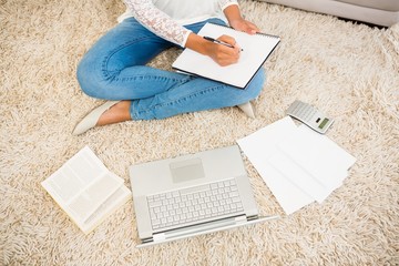 Fototapeta premium Above view of a woman writing note while using her laptop