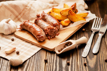 meat with vegetables , fried homemade sausage with roasted potatoes with garlic and pepper on a wooden background