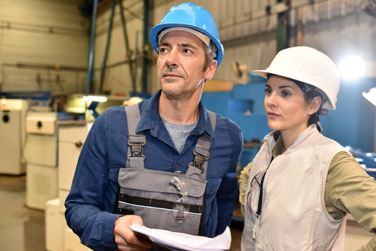 Metal worker showing machine room to apprentice