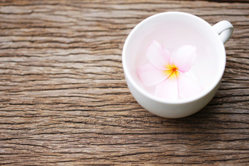Frangipani flower in white cup on wooden table 