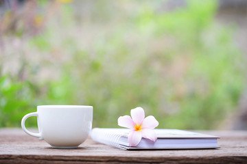 Notebook  and cup with flower on wooden table