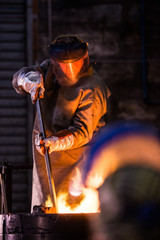 Steel worker in protective clothing raking furnace in an industr