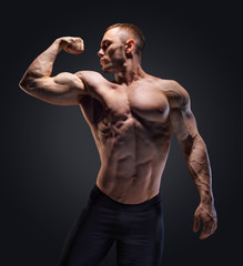 Fototapeta na wymiar Muscular shirtless man in studio over dark background show his muscle.