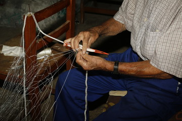 Hombre mayor tejiendo redes de pesca.
