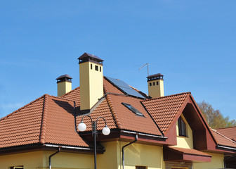 Fototapeta na wymiar Closeup of solar panel on red tiled house roof with skylights, chimney and roof window.